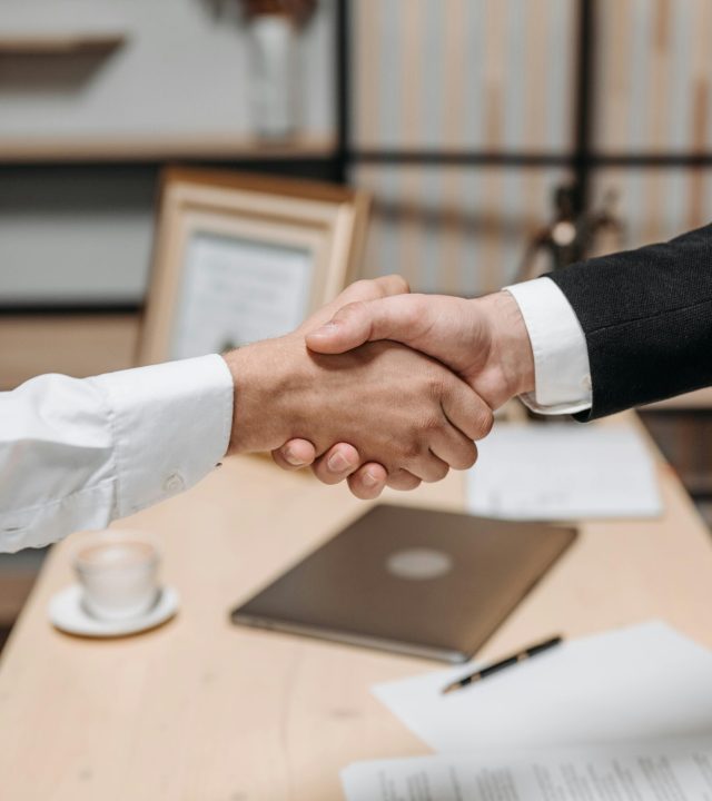 Close-up of two people shaking hands in an office, symbolizing agreement and partnership.